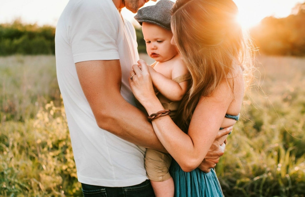 Eltern mit Kind im Arm einer einer Wiese